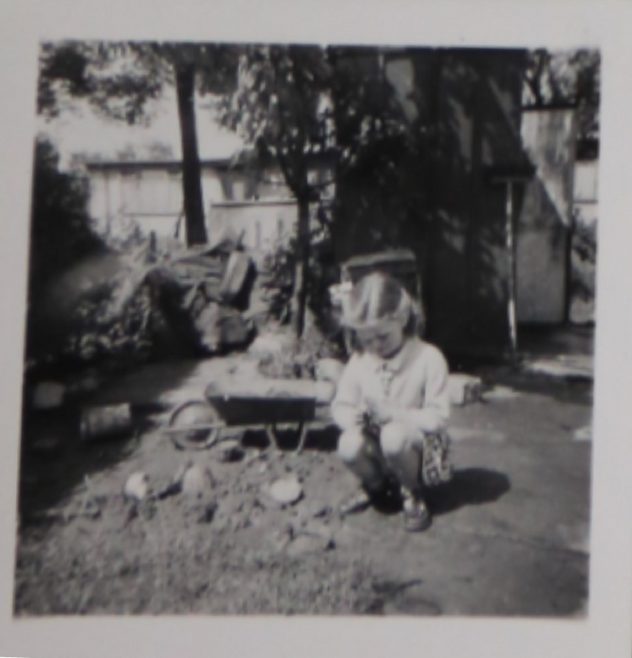 Penny Bishop as a small child playing with a toy wheelbarrow in the prefab garden | Hearn, Jane