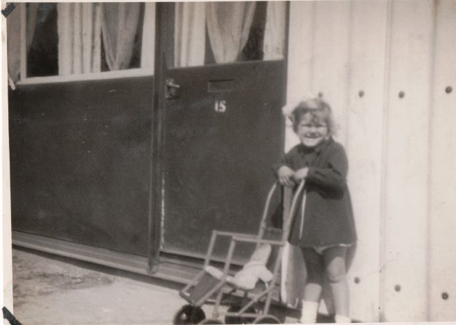 Smail girl with pushchair and doll in front of prefab | Hearn, Jane