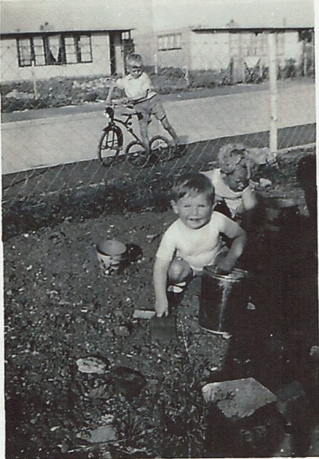 Two small children playing in the prefab garden, one in background on bike | Hearn, Jane