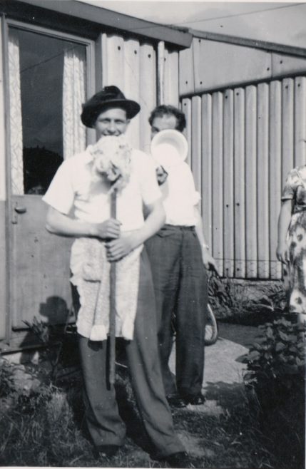 Two men in front of the prefab one holding a mop upside down. Kennylands Road, Hainault