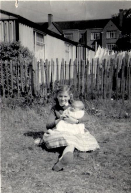 Girl holding baby in the prefab garden. Hollyhedge bungalows, Blackheath, London SE3