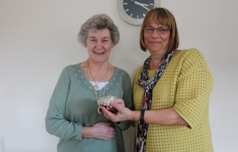 Portrait of Peggy holding a piece of her old prefab, with Siobhan from Rykneld Homes