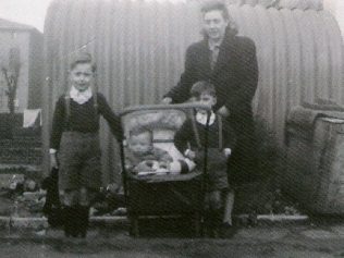 Mum and we three boys, posing outside the Anderson shelter. This would have been in 1948, judging by my physical size in the pram. To the left is the back of a house in Richmond Avenue. | Ray Watts